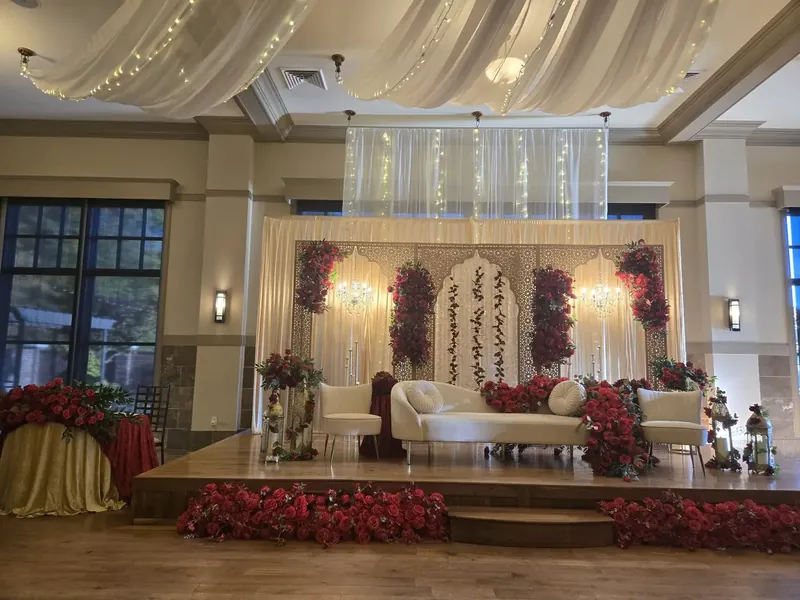 Grand wedding stage with red rose florals, carved ivory panels and ceiling drapery by Events By Maryam