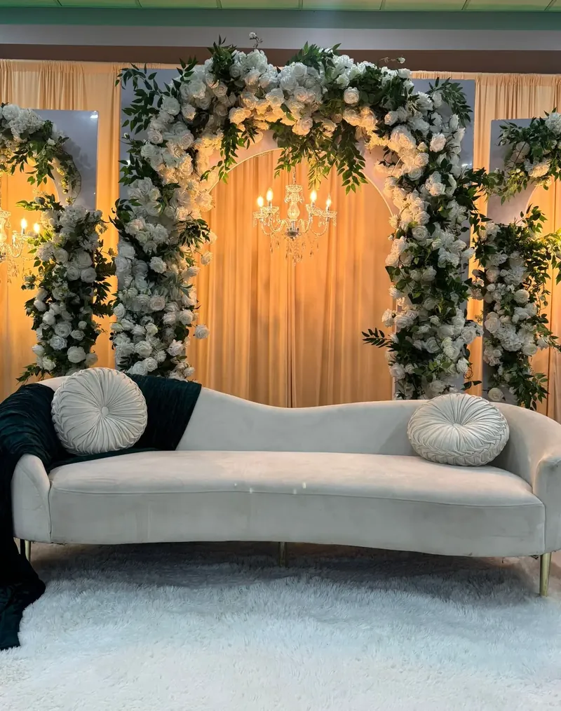 White rose and greenery arches with crystal chandeliers over a curved ivory sofa by Events By Maryam