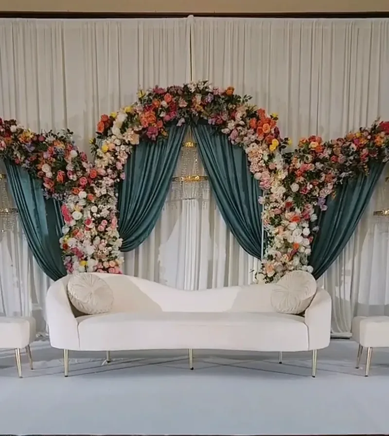 Teal drapery floral arch stage with white sofa by Events By Maryam