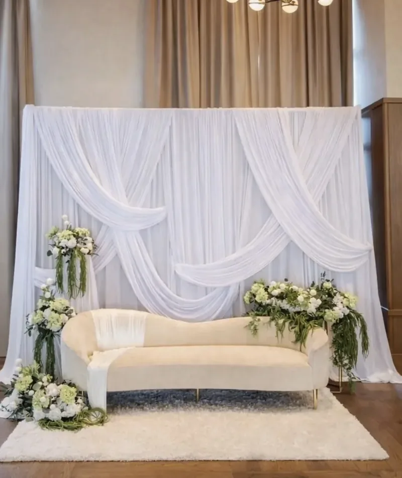 White swag-draped sweetheart stage with ivory chaise and green-and-white florals by Events By Maryam