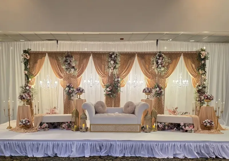 Blush and gold jali-panel reception stage with crystal chandeliers, lanterns and florals by Events By Maryam