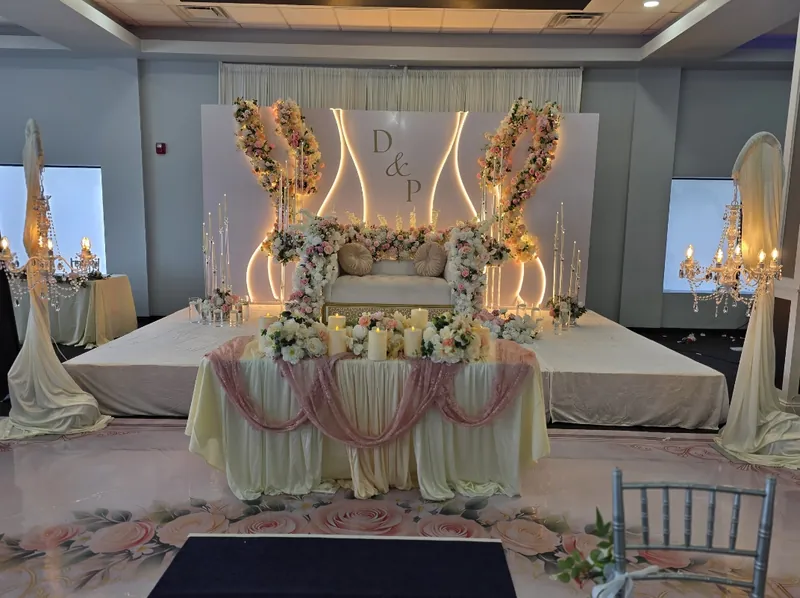 Lit white monogram panel stage with pink-and-white floral arches and candlelit sweetheart table by Events By Maryam