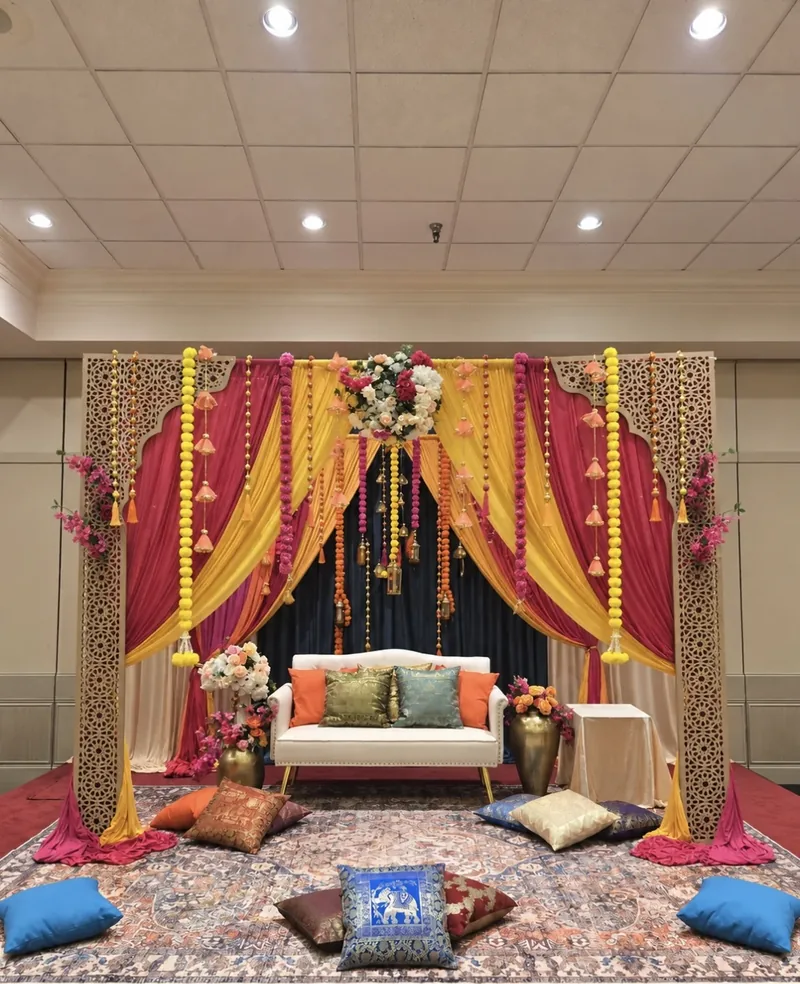 Mehndi stage with jali arches, marigold garlands, jewel drapery and floor cushions by Events By Maryam