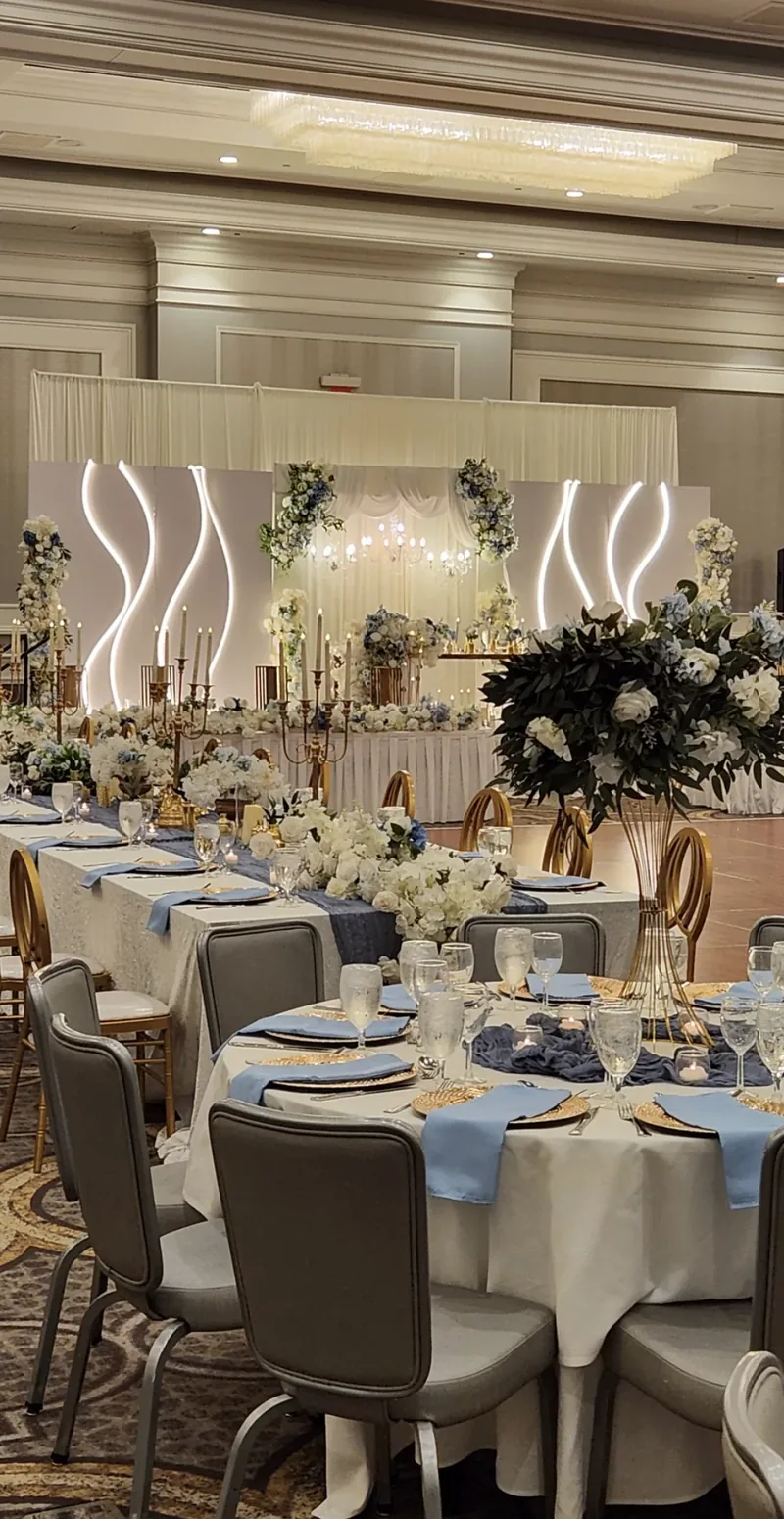 Dusty blue and ivory ballroom reception with lit wave panels, candelabras and floral runners by Events By Maryam