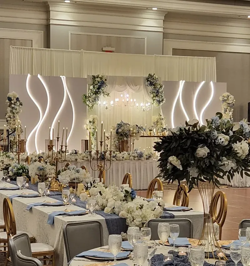 Dusty blue and ivory ballroom reception with lit wave panels, candelabras and floral runners by Events By Maryam