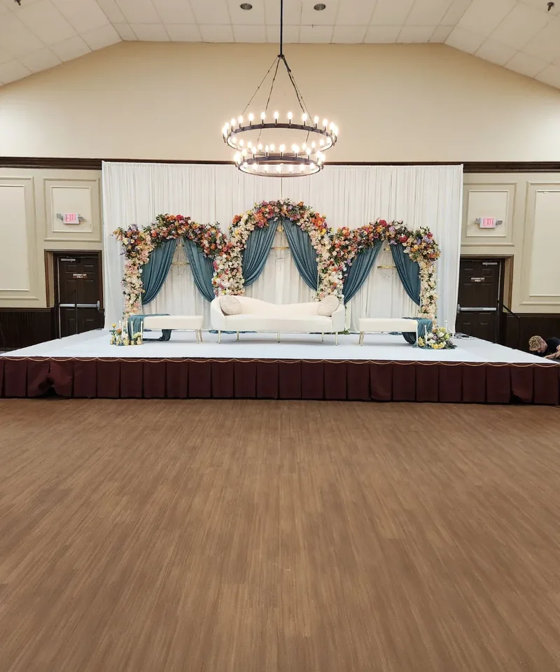 Triple floral arch stage with teal drapery, chandelier and ivory sofa by Events By Maryam