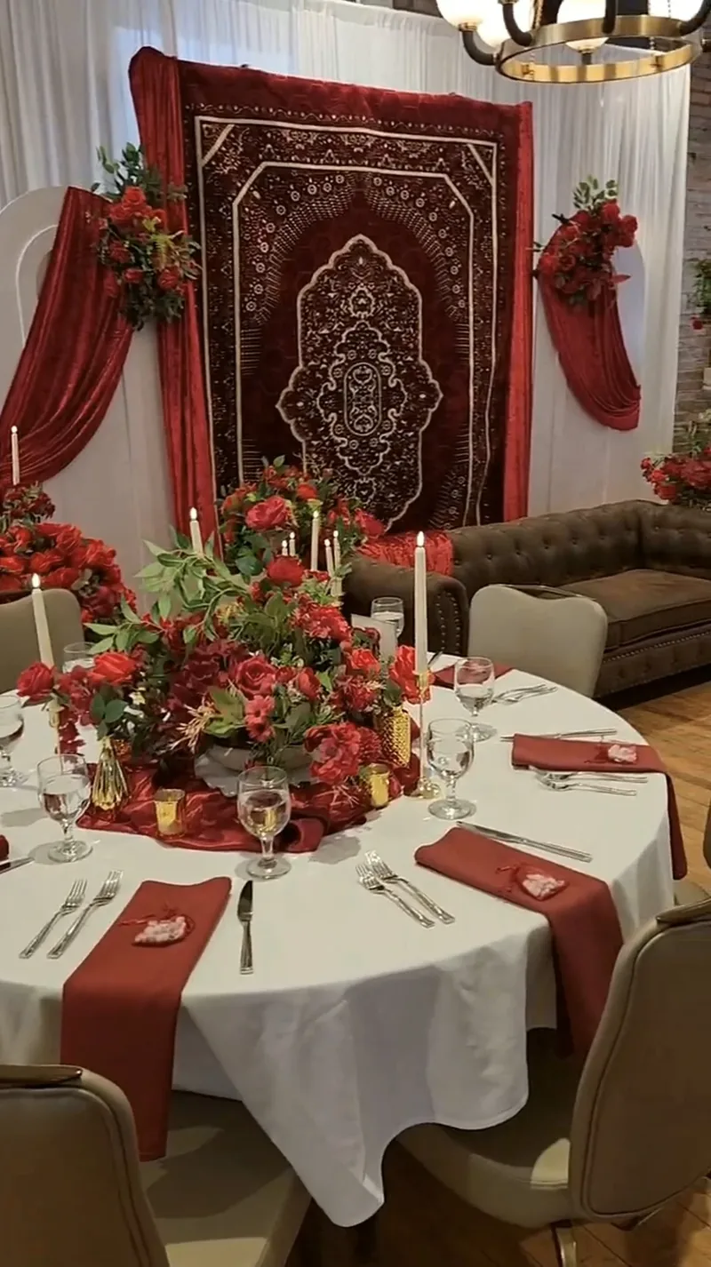 Burgundy rug backdrop with red roses, taper candles and rose centerpiece table by Events By Maryam