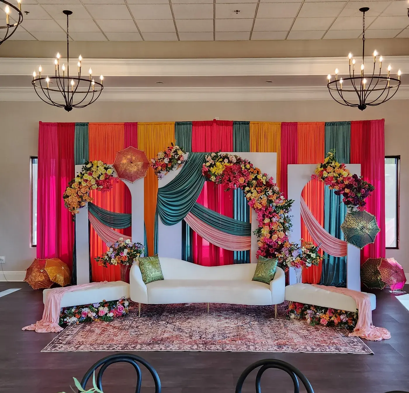 Colorful Mehndi stage with striped drapery, a floral arch and embroidered umbrellas by Events By Maryam